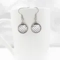 Detailed close up shot of silver fish scale pattern round dangle earrings displayed on white mug. - Silver Holographic