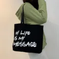 Black canvas tote bag detail view, showing front letter print and sturdy shoulder strap. - Black