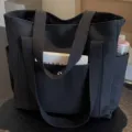 Detail view of the black canvas tote bag showing sturdy double handles and front pocket storage. - Upgraded Style / Black