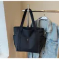 Detail view of black canvas tote bag hanging on rack with denim jacket, large daily commuter bag. - Regular Fit / Black