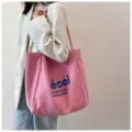Detail shot of a pink canvas tote bag featuring blue printed text, ideal for daily casual use. - Pink