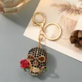 Detailed view of the rhinestone skull keychain with a red rose charm and gold hardware design. - Black