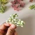 Close up of flocked artificial berry twig, perfect for DIY wreaths and floral craft decor. - White Green