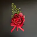 Detailed close-up of a vibrant red artificial corsage flower with green leaves and red ribbon. - Corsage