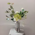Vue détaillée du bouquet de fleurs artificielles blanc et vert dans un élégant vase argenté. - Bouquet + Vase en Céramique Argentée