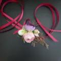 Detail view of artificial flower wrist corsage with pink purple blooms and red ribbons. - Wrist Corsage