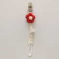 Close-up detail of handmade knitted flower pacifier clip with secure plastic clip and strap. - Red Flower
