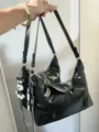 Detailed shot of the minimalist black glossy shoulder baguette bag, featuring a cute charm. - Black