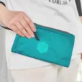 Vue détaillée de la pochette de voyage turquoise avec fermeture éclair et logo. - Bleu lac