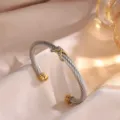 Primer plano de la pulsera de cable de acero con un detalle de cruz de strass dorada. - Plata+Oro
