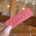 Close-up detail of pink leather hair clip with embossed love text and stitching accent. - Rose Red