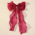 Detail view of a large magenta sheer mesh bow hair clip with long ribbons for elegant styles. - Red