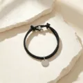 Primer plano detallado de una elegante pulsera de cuero trenzado negro con colgante redondo. - Cuerda Negra Plata