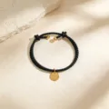 Elegante pulsera de cuero trenzado negro con un colgante redondo dorado minimalista y abalorios. - Cordón Negro Dorado