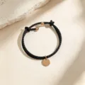 Pulsera de cuero trenzado negro con colgante redondo de oro rosa, detalle de joyería fina. - Cuerda Negra Oro Rosa