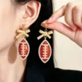 Close-up detail of football dangle earrings with rhinestones, pearls, and gold bow design. - KC Gold
