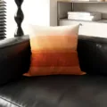 Nahaufnahme des lebendigen Ombre-Zierkissens auf Ledersofa vor modernem Regalhintergrund. - Orangeroter Sonnenuntergang