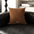Detailaufnahme des braunen Dopamin-Quadratkissen mit Keksmuster auf schwarzem Ledersofa. - Braune Kaffeelinie