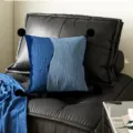 Detail shot of blue color-blocked throw pillow with black pom-poms on dark leather sofa. - Foggy Blue Pattern Black Pom-pom
