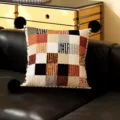 Detailed view of a retro geometric throw pillow with black pom-poms on a modern black leather sofa. - Dusk Terrace Black Pom-Pom