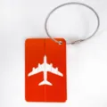 Orange aluminum luggage tag with steel wire loop and airplane cutout design for travel bags. - Orange