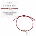 Adjustable red string evil eye bracelet with hamsa hand charm and tassel on backing card. - Red