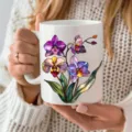White ceramic coffee mug with colorful stained glass orchid design held in hands, closeup view - 301-400ml / Orchid Print / White