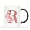 Nahaufnahme Detail einer Keramiktasse mit rosegoldenen Buchstaben R und rosa Magnolienblüten. - Buchstabe R