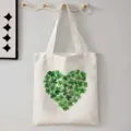 Detailansicht der weißen Canvas-Tragetasche mit grünem Kleeblatt-Herz-Print an Wandhaken. - 42cm*35cm / Kleeblatt Herz Druck