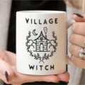 Nahaufnahme einer weißen Keramiktasse mit süßem Hexendorf Motiv und schönem Schriftzug. - Stil 12