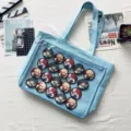Detail view of light blue canvas ita bag featuring clear window and anime character pins inside. - Light Blue