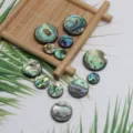 Vue détaillée de pendentifs ronds en coquillage abalone avec texture de perle irisée. - 6mm / Coloré