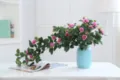 Detailed view of artificial pink rose vine flowers in a blue ceramic vase for home decor. - Purple Pink