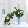Artificial white flower vine cascading in a blue vase, perfect for home and wedding decor. - White