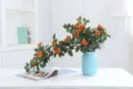 Detailed view of artificial orange rose vine in a light blue vase for home decor setup. - Orange