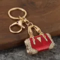 Close-up detail of luxury red enamel rhinestone handbag keychain metal charm pendant accessory. - KC Gold + Red