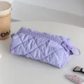 Detailed view of a pastel purple quilted cosmetic bag featuring glossy fabric and an oversized zipper. - Purple