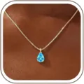 Close-up of a pear-cut blue cubic zirconia pendant necklace on a delicate gold box chain. - 14k / December - Gold