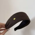 Vista detallada de la diadema ancha marrón con una elegante etiqueta de marca de metal dorado. - Marrón