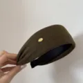 Detalle de diadema ancha de lana verde oscura con una placa de logotipo de metal dorado. - Verde