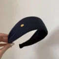 Primer plano detallado de la diadema ancha de tela azul marino con un elegante logo dorado. - Azul Oscuro