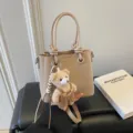 Elegante beigefarbene Pendlerhandtasche aus strukturiertem Leder mit süßem Bärenanhänger. - Mit Anhänger / Aprikose