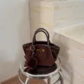 Brown suede handbag detail, featuring double top handles, metal clasp and plush pompom charm. - No Pendant / 16x8x15 / Coffee