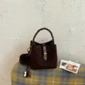 Vista di dettaglio della borsa a secchiello in camoscio marrone scuro con manico intrecciato. - Caffè