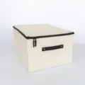 Beige stoffen opbergdoos met rits en handvat voor kleding en dekens in de slaapkamer thuis. - Beige