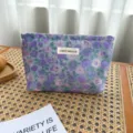 Detailed view of the purple floral woven cosmetic bag with brand label and fine texture. - M / Purple Floral