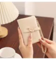 Detail shot of a minimalist beige short wallet with a chic leaf metal buckle and hand strap. - Apricot