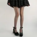 Close-up detail shot of sparkling black sheer pantyhose featuring shimmering dots on legs. - One Size / Black