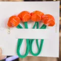 Detailed close-up of orange faceted star hair ties with green elastic bands on a white card. - Orange