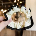 Close-up detail of the elegant black and white ruffled satin hair scrunchie accessory. - Beige Black Trim